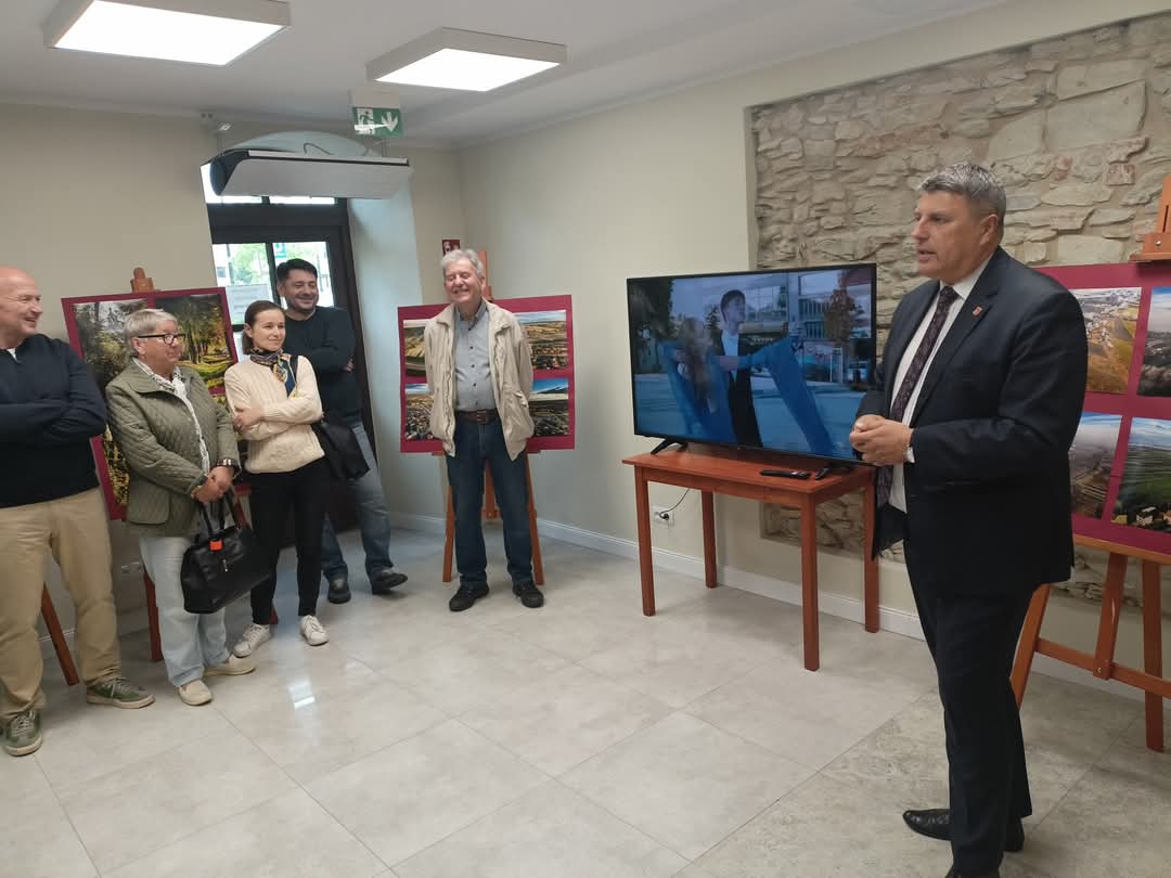 uczestnicy spotkania słuchają przemowy burmistrza, w tle sztalugi z fotografiami